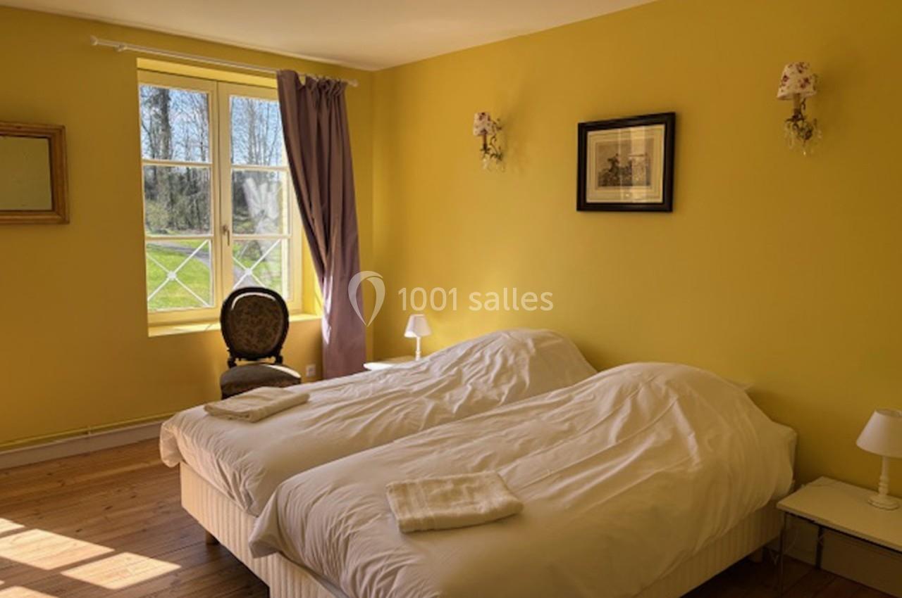 Deux lits simples avec draps blancs dans une chambre lumineuse aux murs jaunes, vue sur un jardin par une fenêtre.