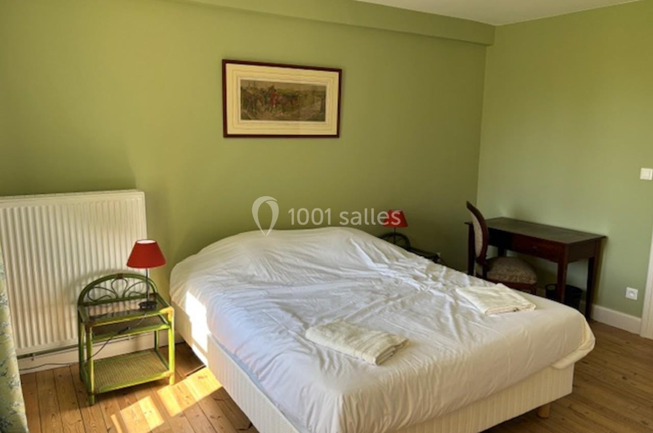 Chambre avec lit double, murs verts, bureau en bois, deux lampes rouges et parquet en bois clair.