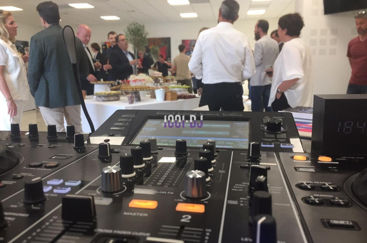 Vue d'une table de mixage au premier plan lors d'un événement avec des invités debout autour d'un buffet.