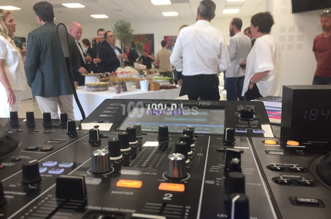 Vue d'une table de mixage au premier plan lors d'un événement avec des invités debout autour d'un buffet.