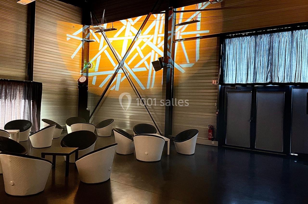 Salle moderne avec des fauteuils blancs, éclairage mural géométrique orange et rideaux couvrant des fenêtres.