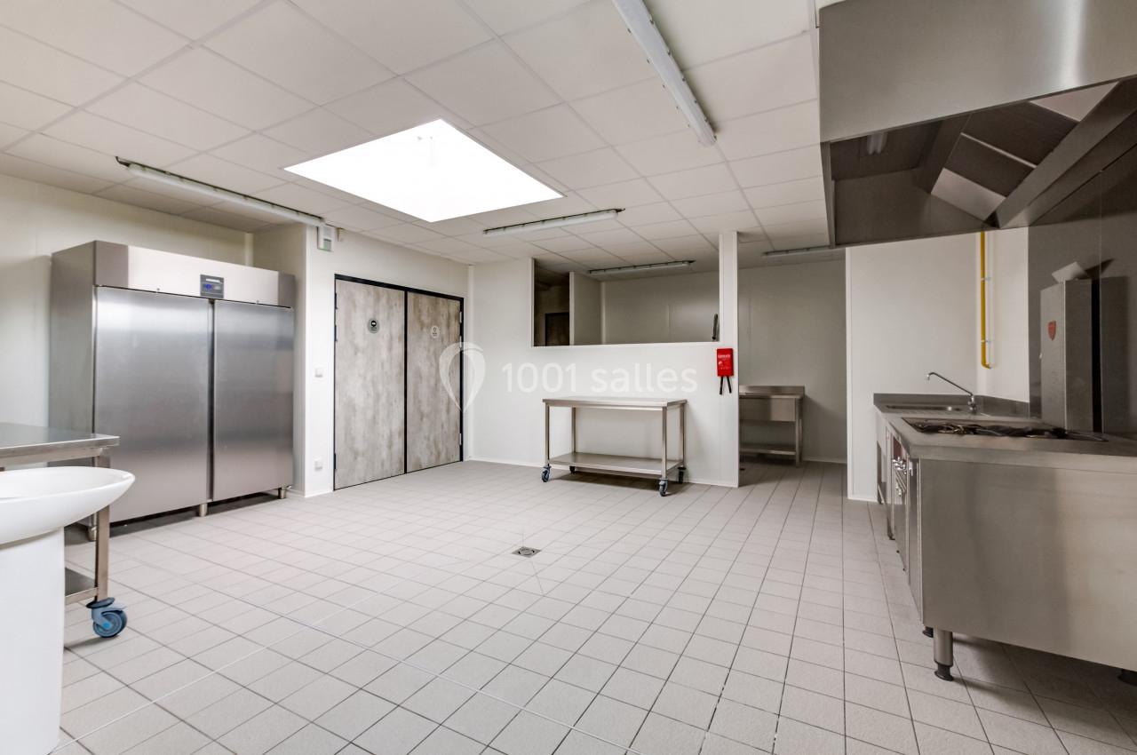 Cuisine professionnelle vide avec équipements en inox, sol carrelé, éclairage naturel et portes de stockage visibles.
