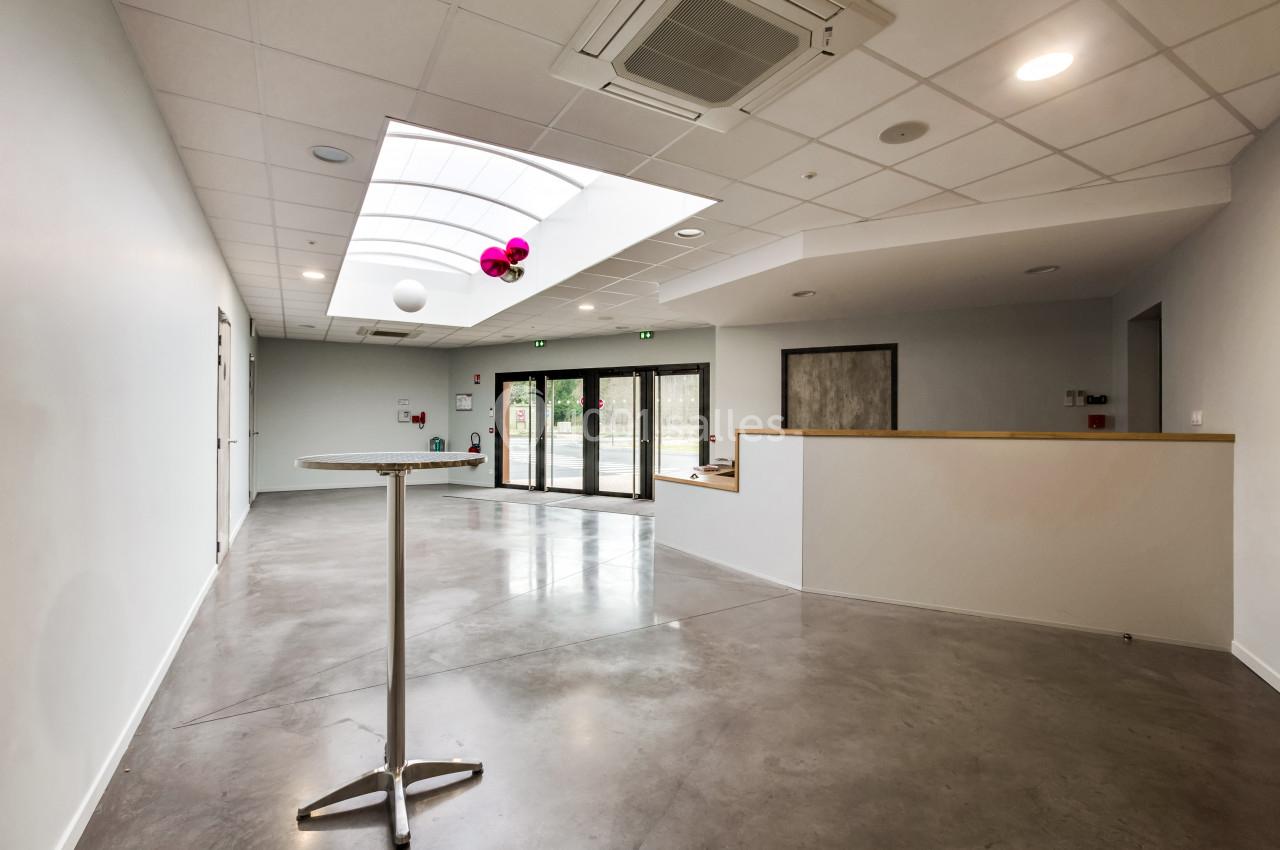 Salle lumineuse avec sol en béton, plafond à dalles blanches, grande baie vitrée et table haute en métal.