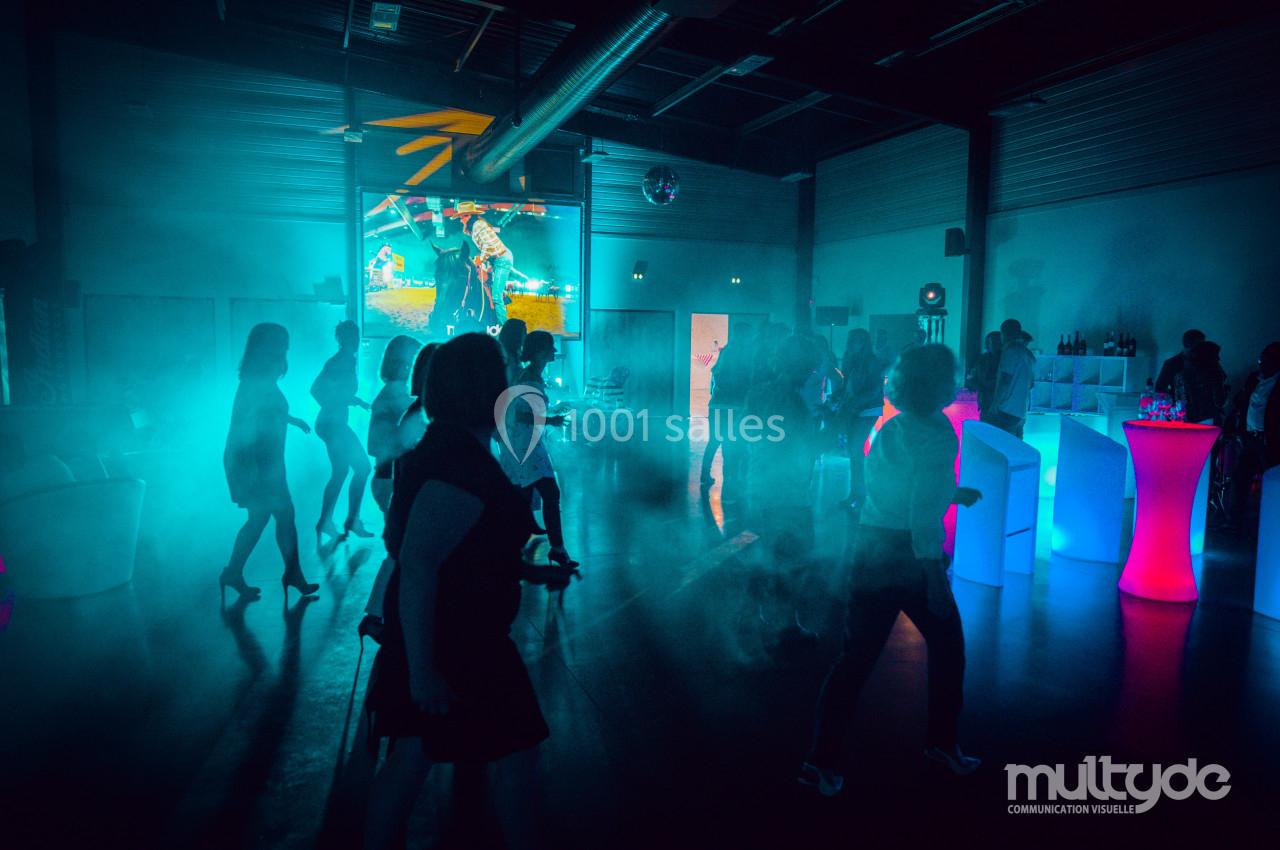 Des personnes dansent dans une salle sombre éclairée par des lumières colorées et des effets de fumée.