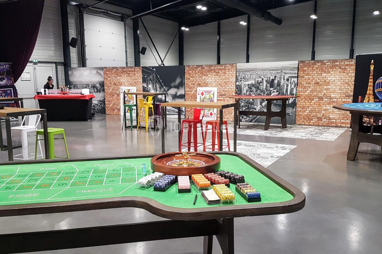Salle aménagée avec des tables de jeux de casino, des chaises colorées et un décor mural urbain.