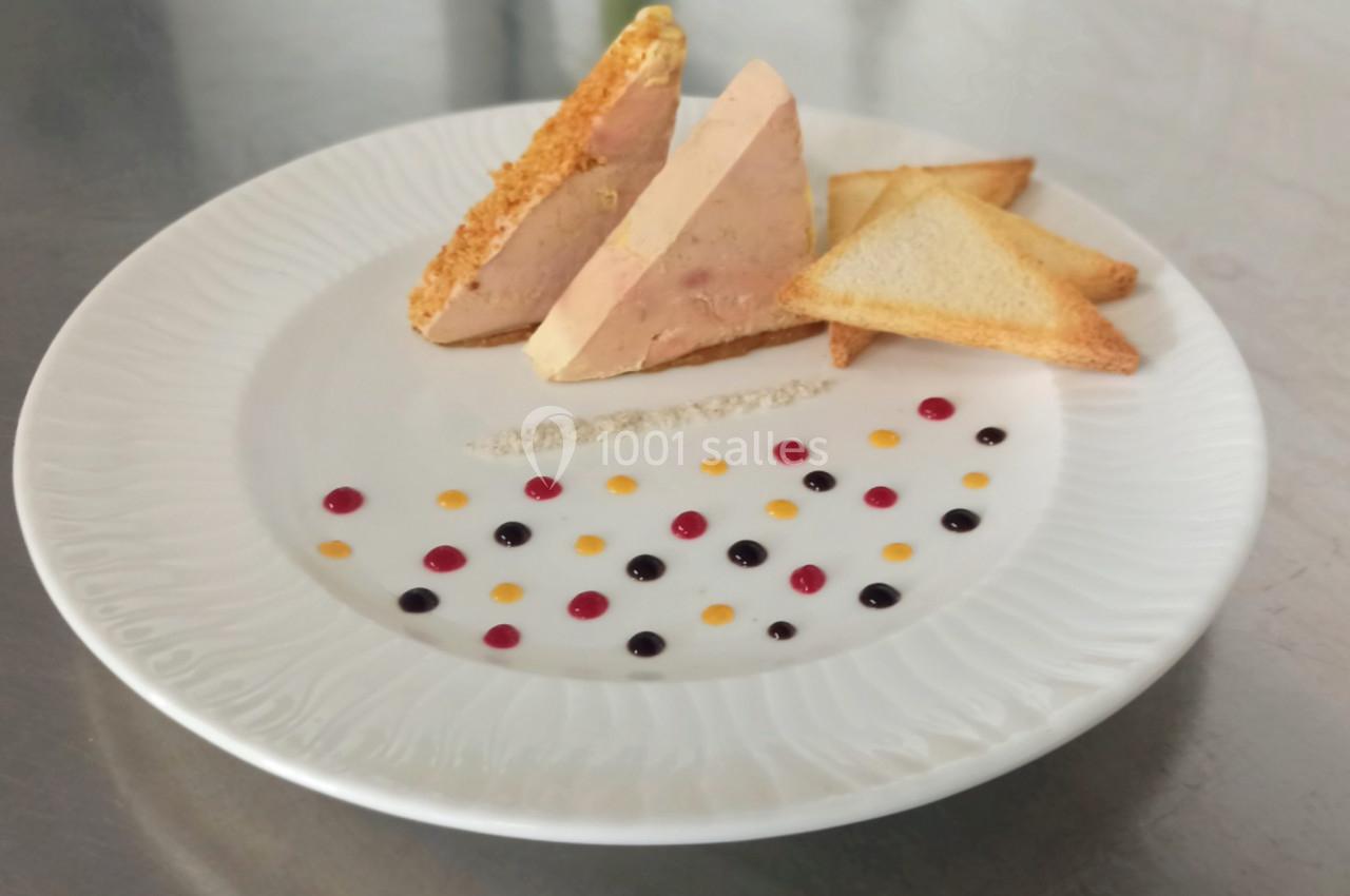 Assiette de foie gras en tranches avec toasts triangulaires et décor de sauces colorées sur une table en métal.