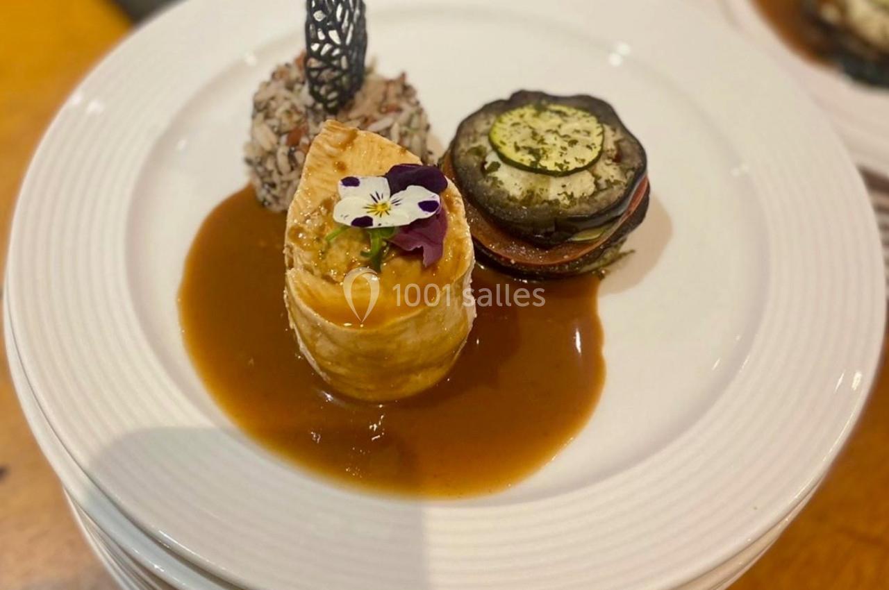 Assiette gastronomique avec feuilleté garni, légumes grillés, riz en boule et sauce, décorée d'une fleur comestible.