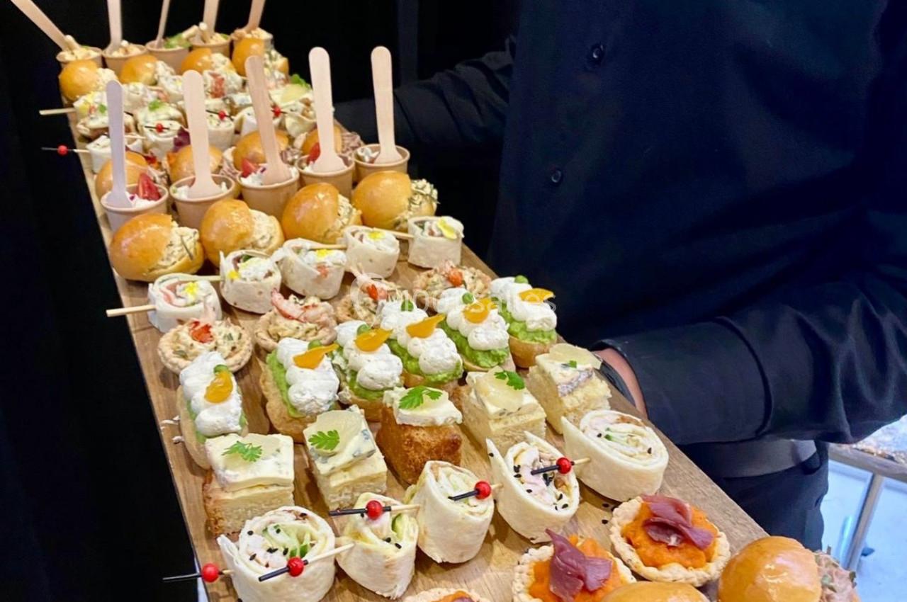 Plateau de bouchées apéritives variées, présenté par une personne en tenue professionnelle.