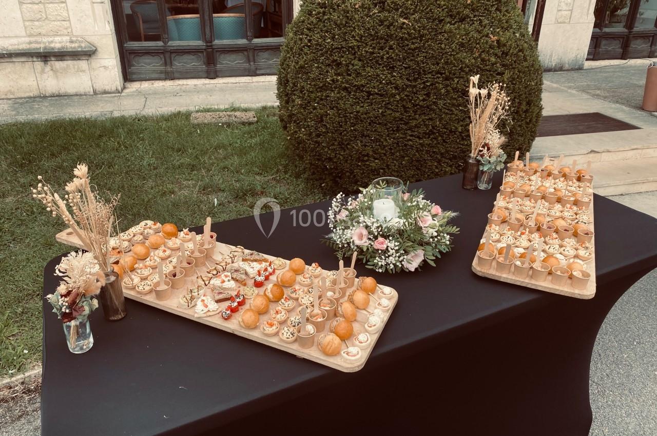 Plateau de petits fours variés disposés sur une table noire en extérieur, avec des décorations florales et végétales.