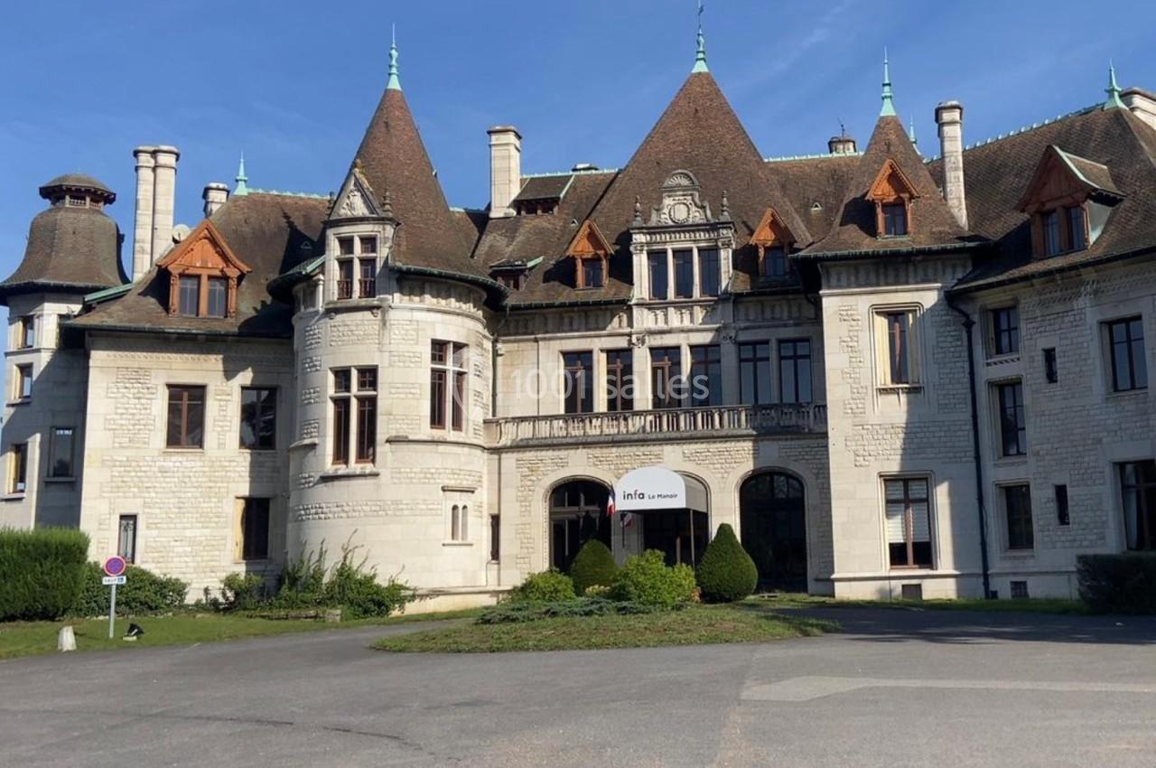 Façade d'un grand bâtiment historique en pierre avec plusieurs tours et toits en pente sous un ciel bleu.