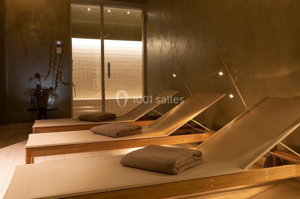 Chaises longues en bois avec serviettes pliées dans une pièce tamisée, éclairée par des lampes et une lumière douce.