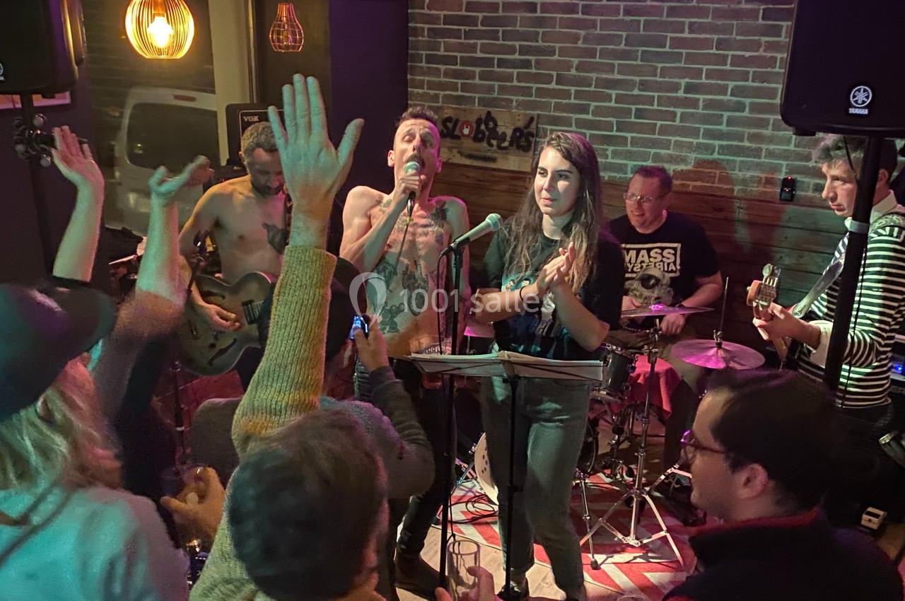Un groupe de musiciens joue sur scène dans un bar animé, entouré d'un public enthousiaste.