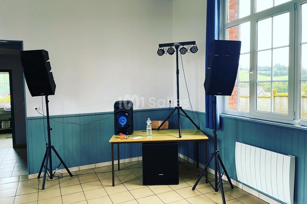 Matériel de sonorisation et éclairage installé dans une salle avec table, chaises et fenêtre donnant sur l'extérieur.