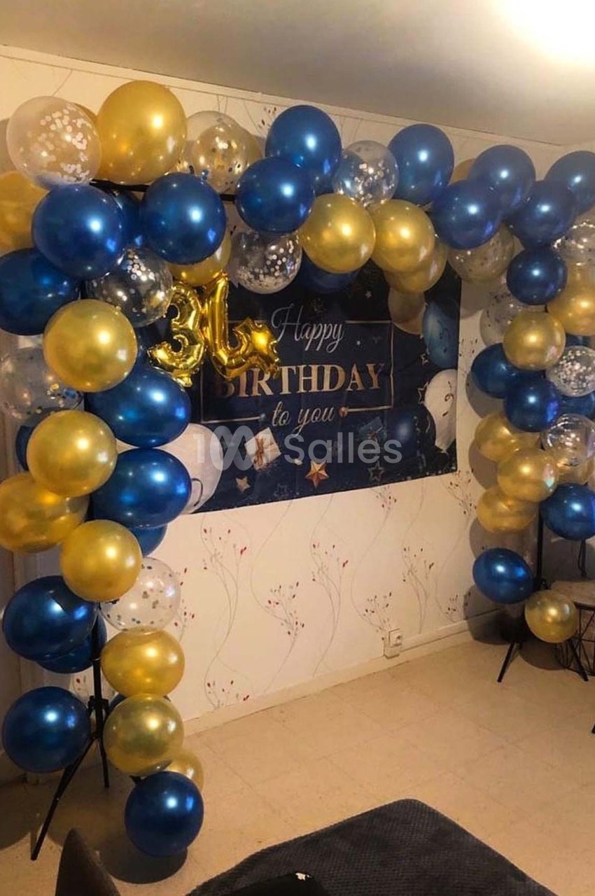 Arche de ballons bleus, dorés et transparents décorant une pièce avec une bannière d'anniversaire en arrière-plan.