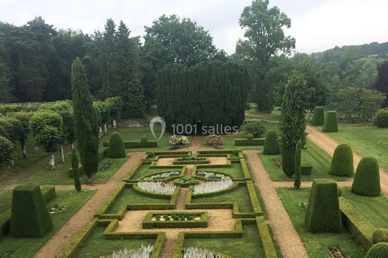 Jardin à la française avec parterres symétriques, allées de gravier et arbustes taillés, entouré de verdure.