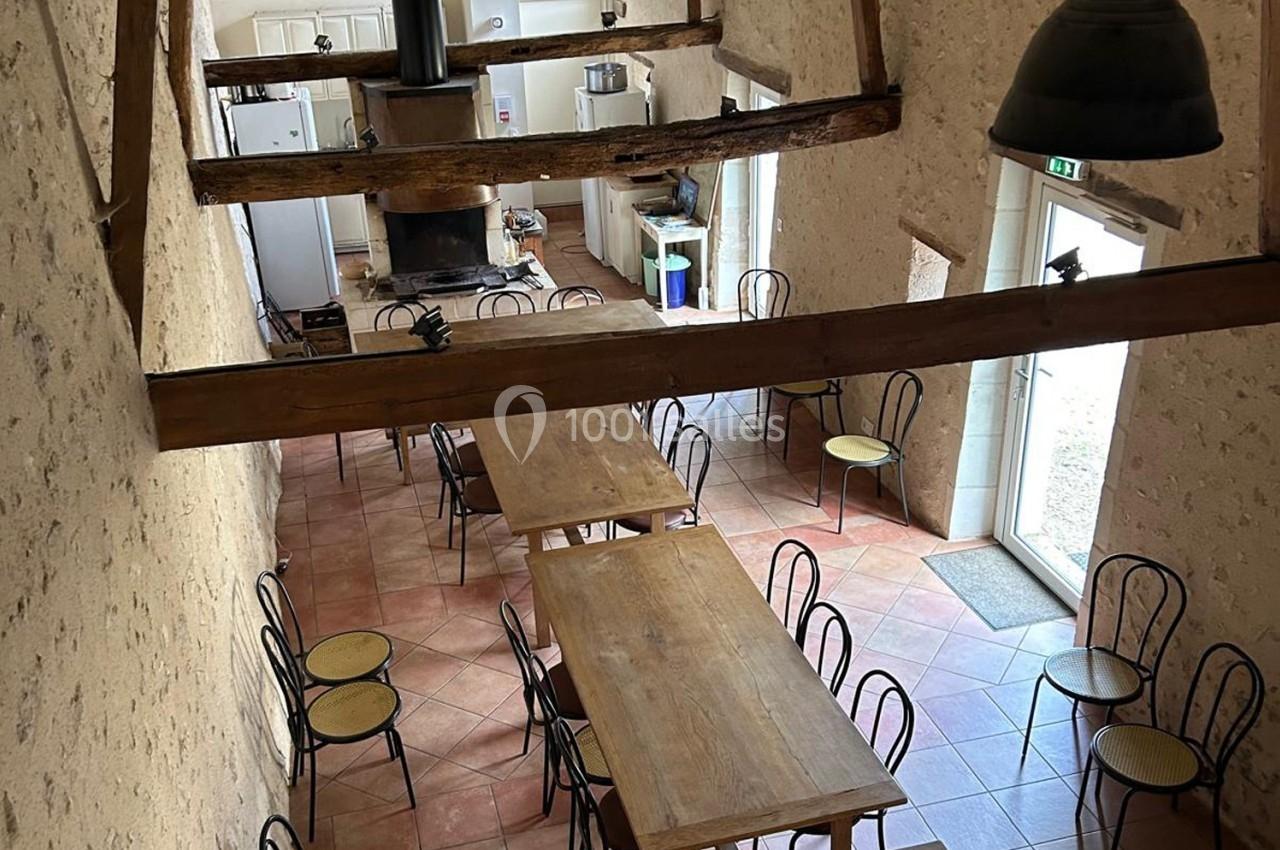 Salle à manger rustique avec tables en bois, chaises en métal et poutres apparentes, vue depuis une mezzanine.