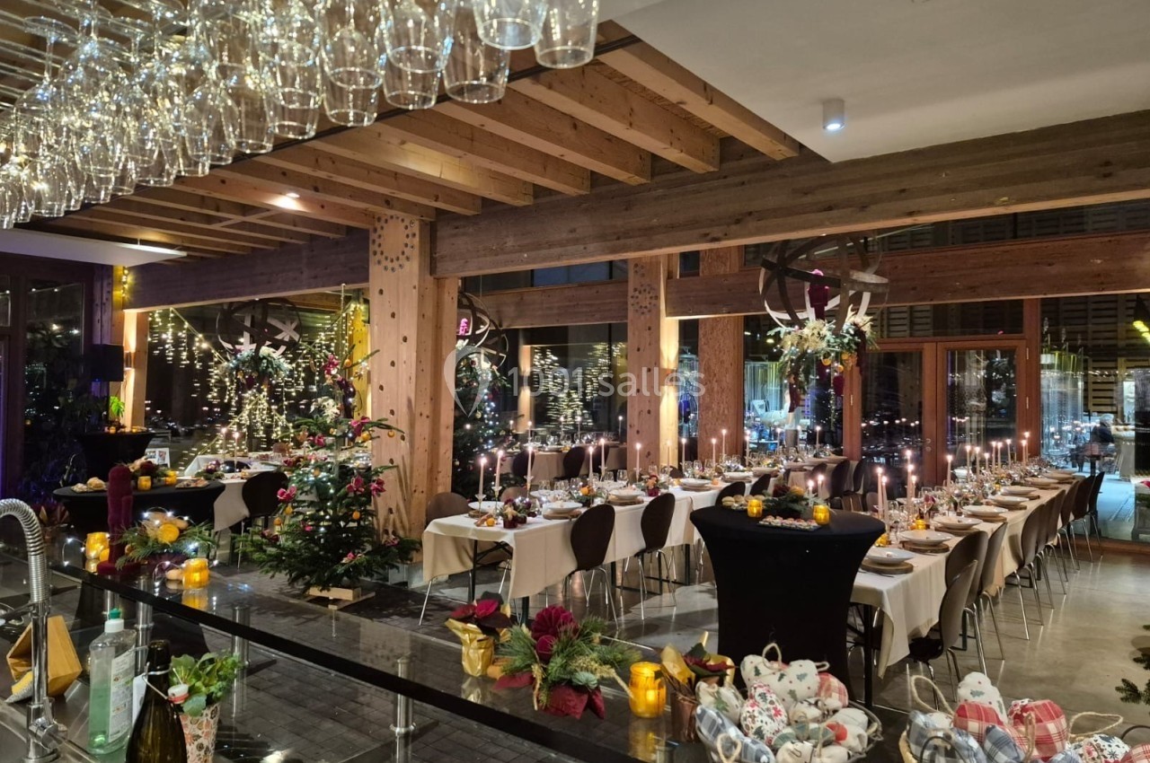 Salle de réception décorée pour un dîner festif, avec tables dressées, bougies allumées et sapin de Noël illuminé.