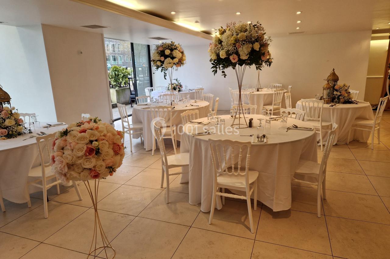 Salle de réception décorée avec des tables rondes, nappes blanches et arrangements floraux élégants.