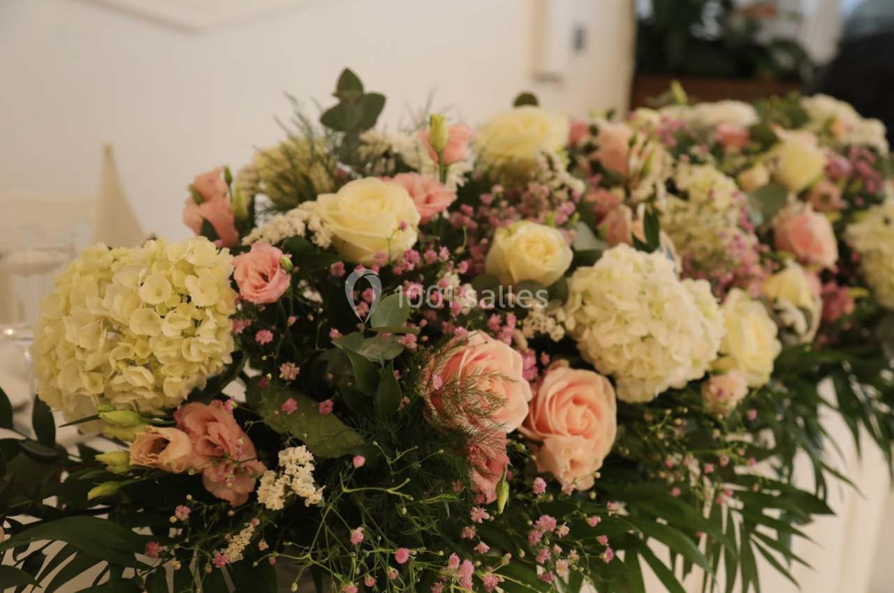 Arrangement floral composé de roses, d'hortensias blancs et de petites fleurs roses, entouré de feuillage vert.