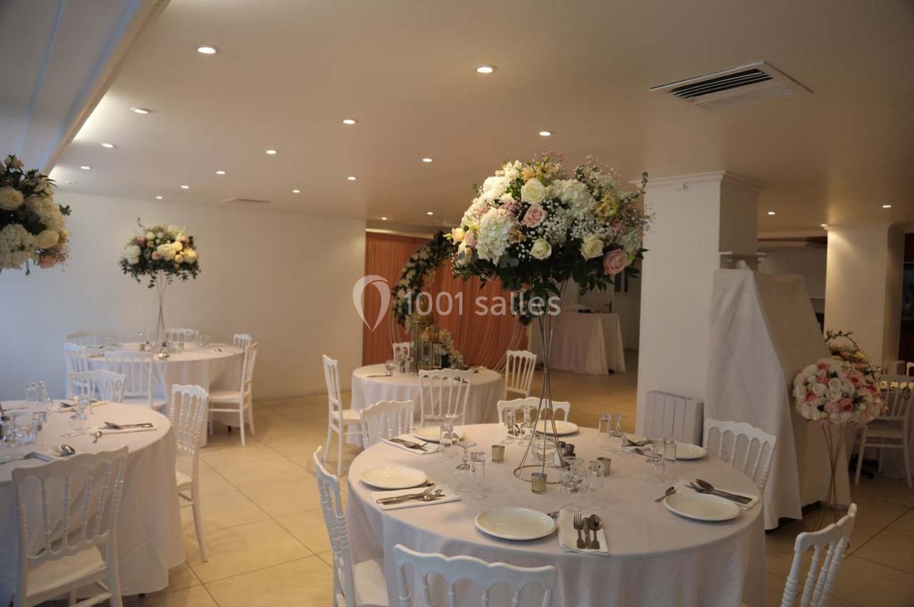 Salle de réception décorée avec des tables rondes, nappes blanches, chaises assorties et compositions florales élégantes.