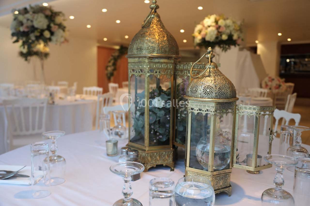 Décoration de table avec lanternes dorées, fleurs et verrerie dans une salle de réception élégamment éclairée.