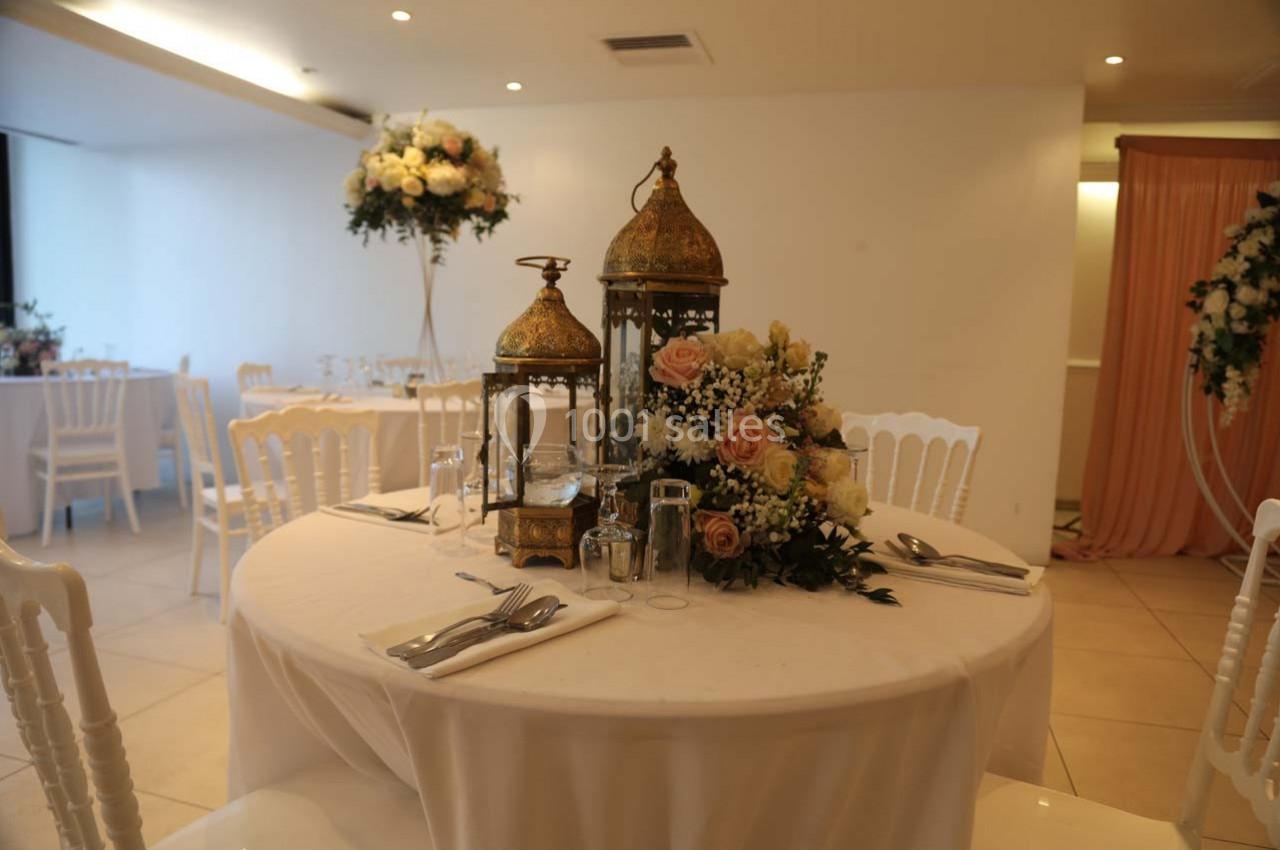 Table décorée avec des lanternes dorées, des fleurs pastel et des couverts, dans une salle de réception lumineuse.