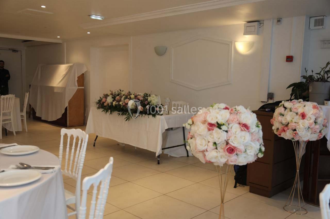 Salle décorée pour un événement avec des tables dressées, des compositions florales et des chaises blanches.