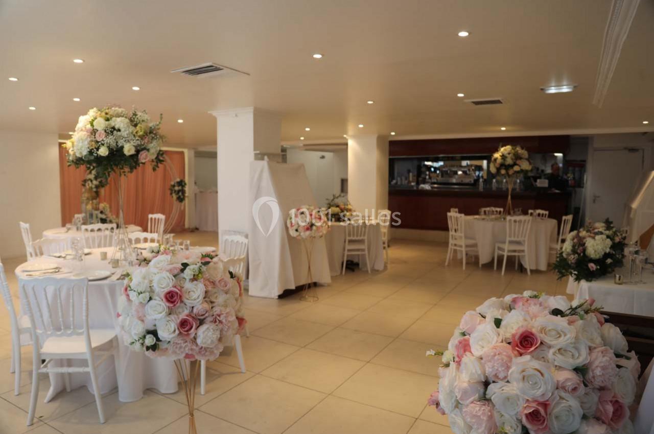 Salle de réception lumineuse avec tables décorées de nappes blanches et compositions florales aux tons pastel.