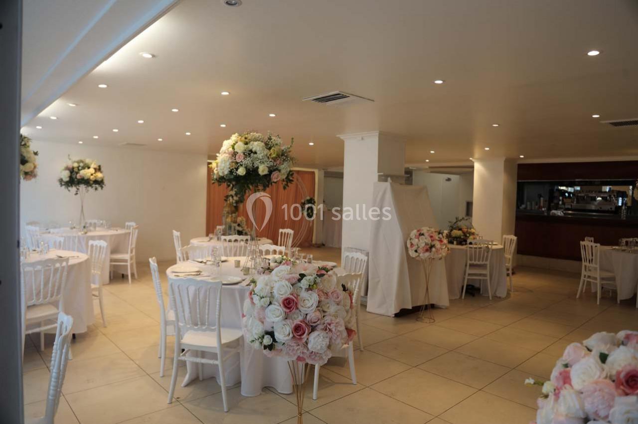 Salle de réception décorée avec des tables rondes, des chaises blanches et des arrangements floraux élégants.