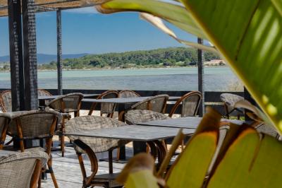 Miniature Location salle Six-Fours-les-Plages (Var) - La Lagune #2 Vue d'une plage avec une terrasse ombragée, des promeneurs, une étendue d'eau et des collines à l'horizon.