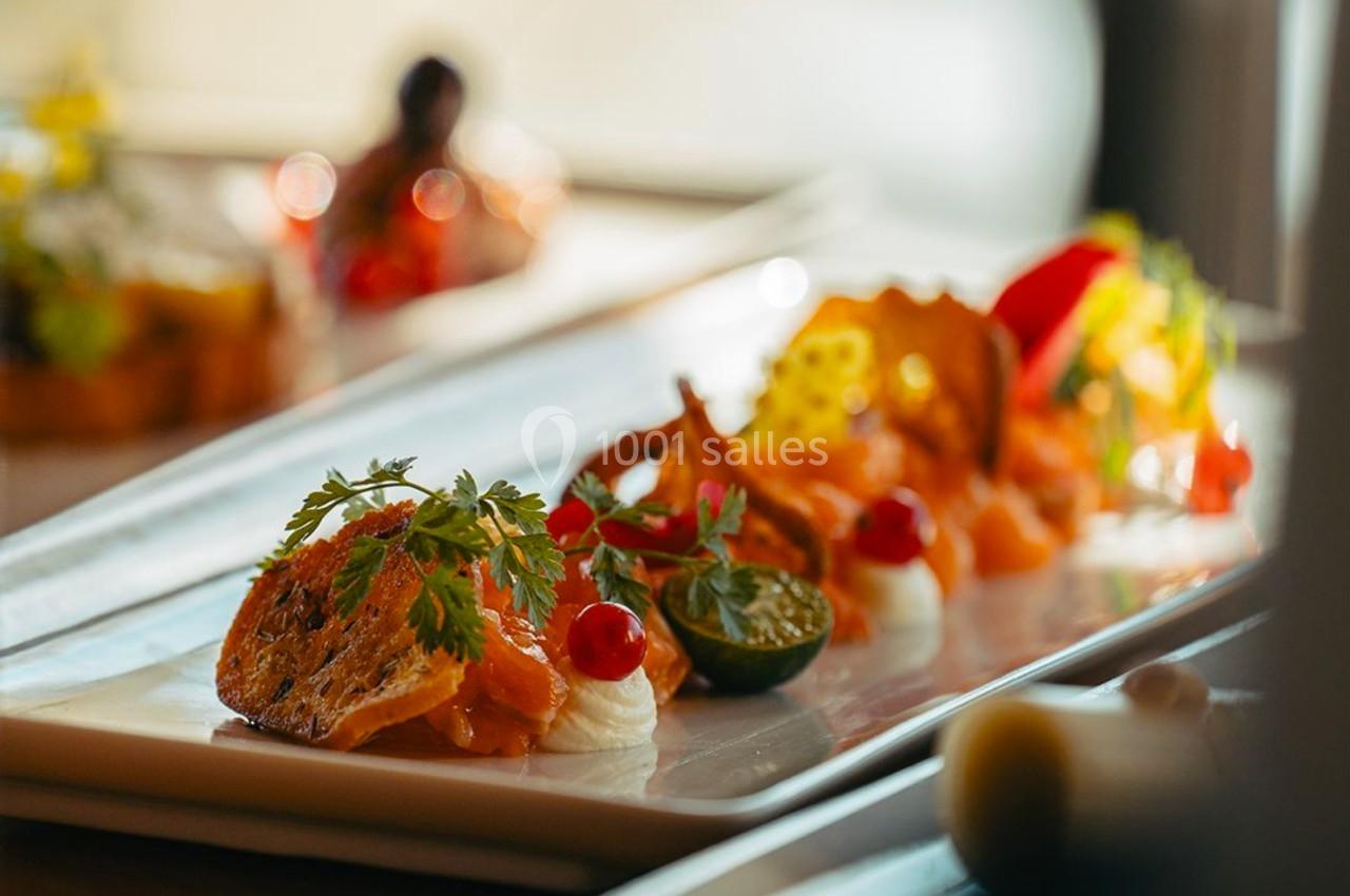 Assiette gastronomique avec des portions de saumon, crème, herbes fraîches et légumes, présentée sur une table lumineuse.