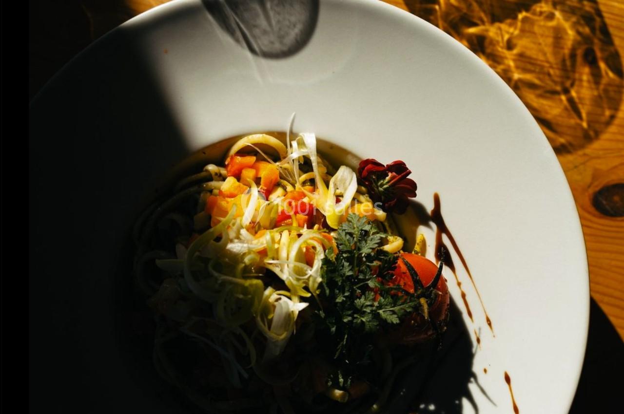 Assiette de pâtes garnie de légumes colorés et herbes fraîches, éclairée par une lumière naturelle partielle.