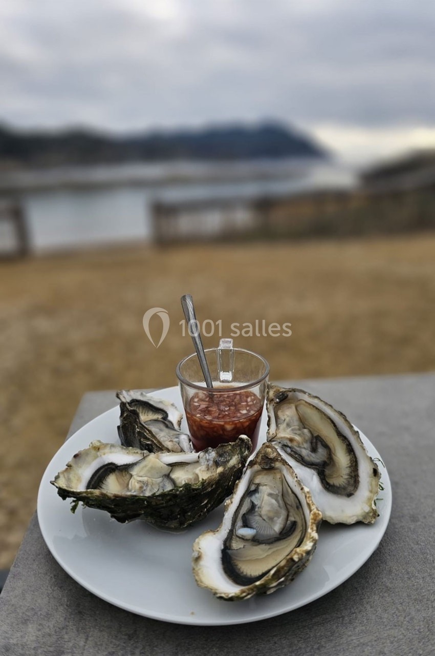 Assiette d'huîtres ouvertes avec une sauce à l'échalote en bord de rivière sous un ciel nuageux.