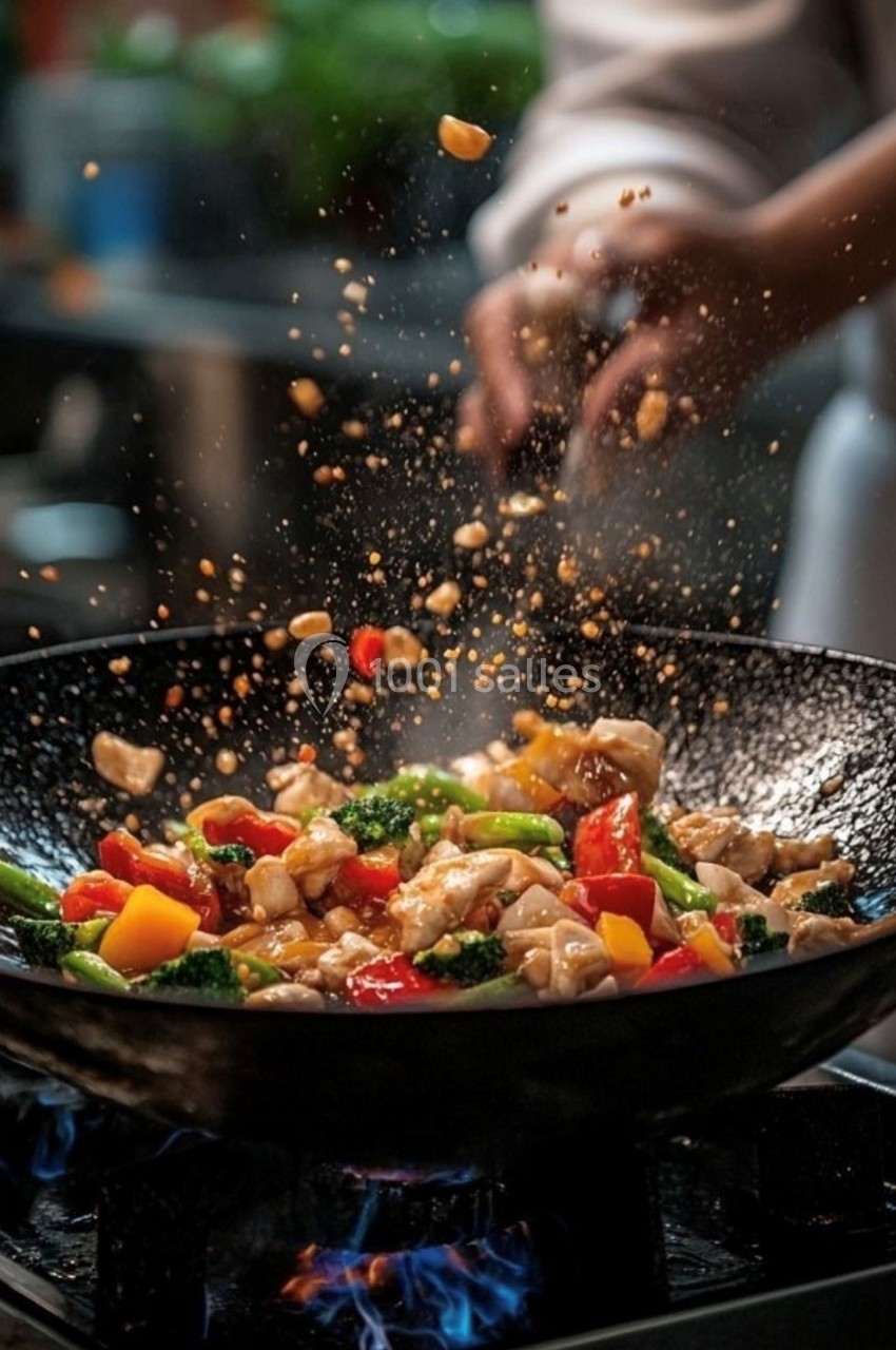 Légumes colorés et morceaux de poulet sautés dans un wok, avec des flammes visibles en dessous.
