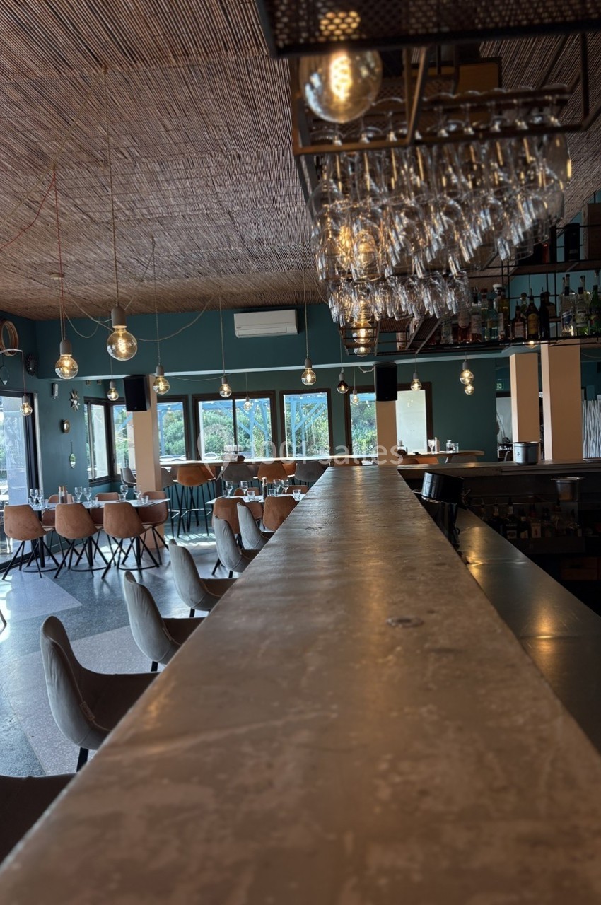 Intérieur d'un restaurant avec bar en premier plan, tables et chaises en arrière-plan sous un plafond en bois.