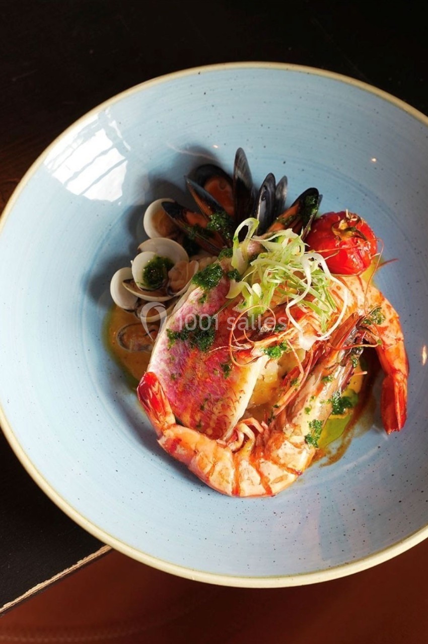 Assiette de fruits de mer avec poisson, crevettes, moules, palourdes et légumes, servie dans une sauce colorée.