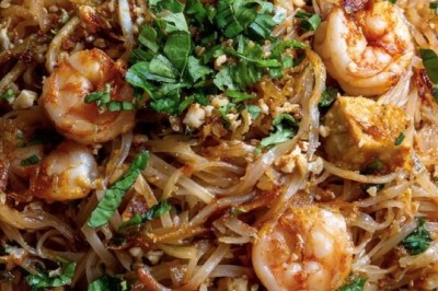 Assiette de pad thaï avec crevettes, tofu, coriandre, cacahuètes concassées et quartiers de citron vert.