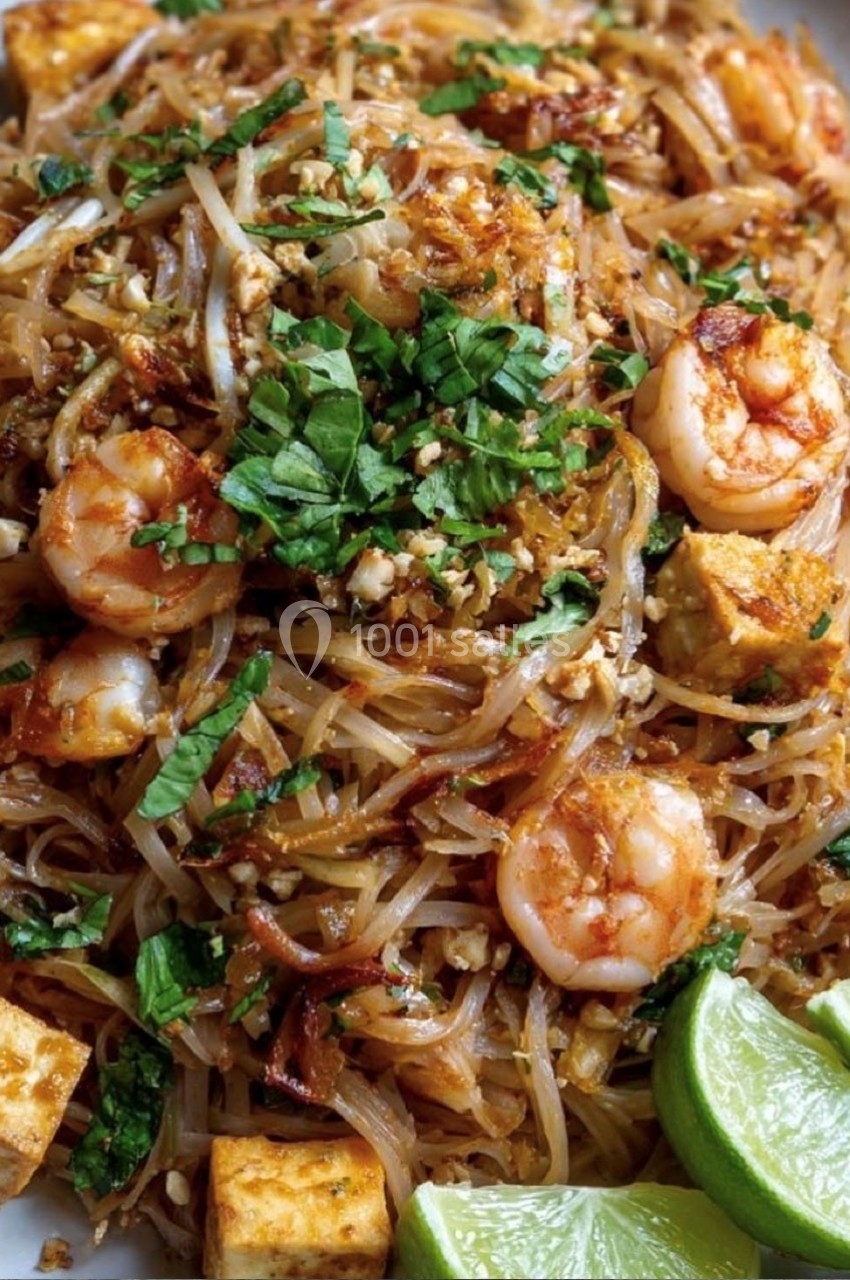 Assiette de pad thaï avec crevettes, tofu, coriandre, cacahuètes concassées et quartiers de citron vert.