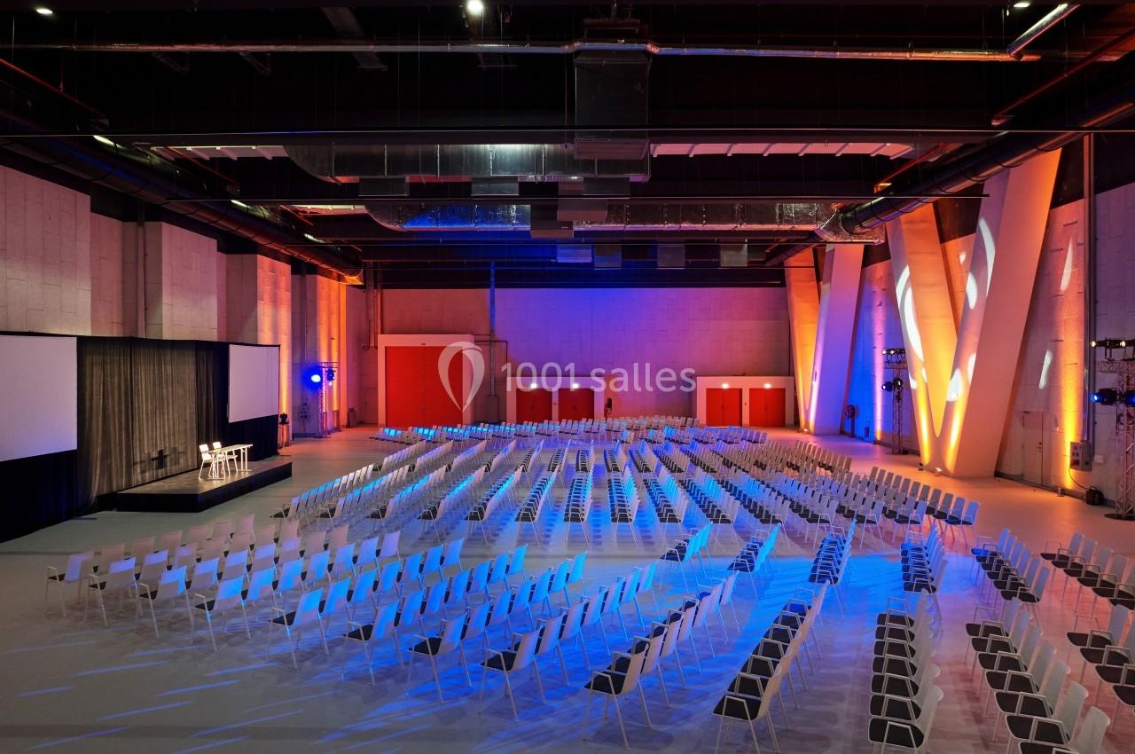 Salle de conférence vide avec des rangées de chaises alignées, un podium et deux écrans de projection.