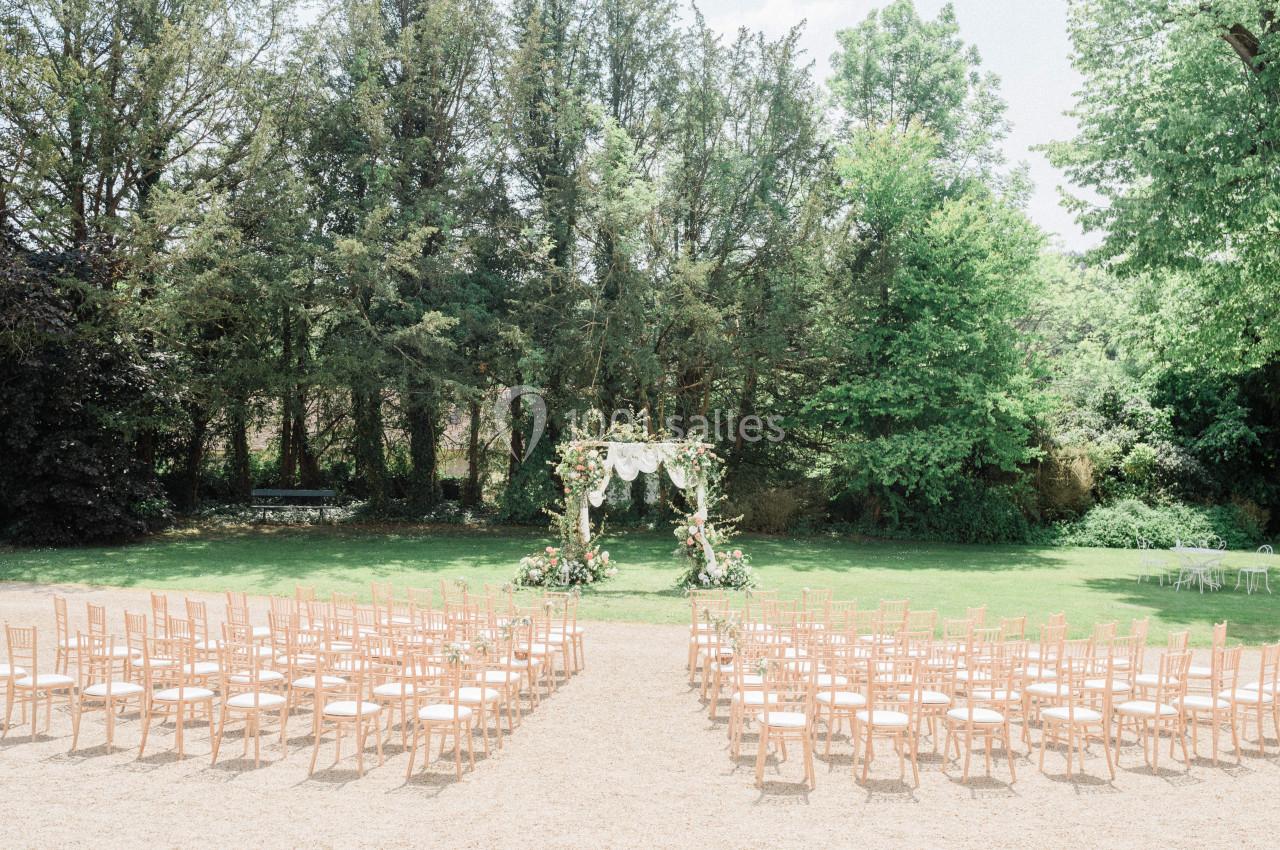 Chaises disposées en rangées face à une arche décorée de fleurs dans un jardin verdoyant pour une cérémonie en plein air.