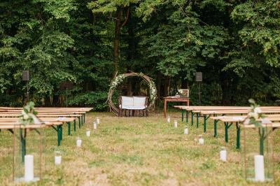 Femme en veste rouge lisant un texte sur un pupitre décoratif, devant un mur en pierre.