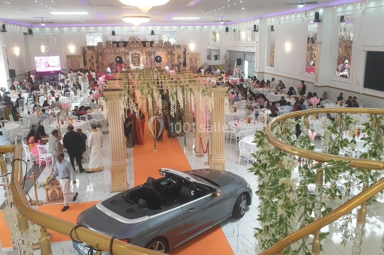 Salle de réception décorée pour un événement, avec une voiture décapotable grise au premier plan et des invités assis.