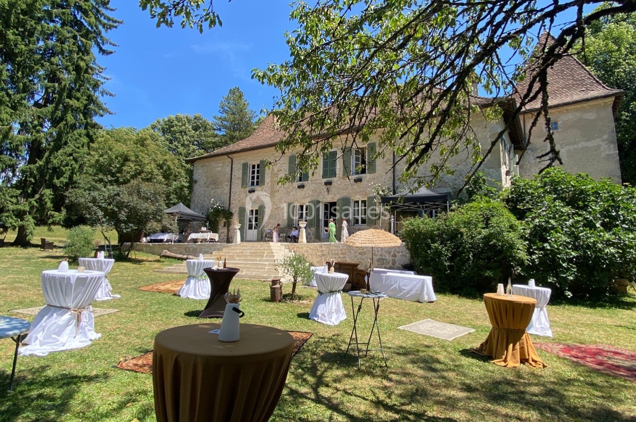 Jardin d'une maison en pierre avec tables dressées pour un événement en plein air, sous un ciel bleu.