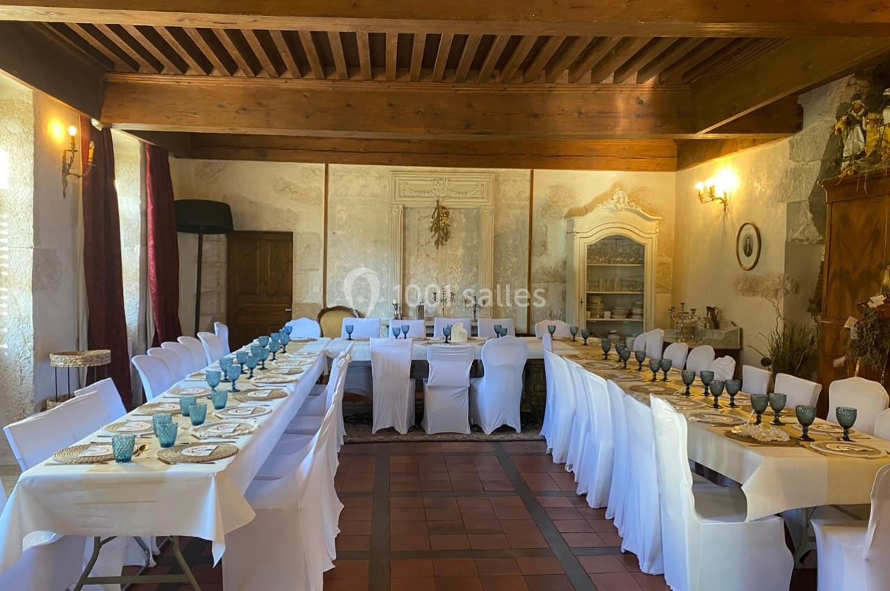 Salle de réception avec tables dressées en U, nappes blanches, chaises houssées et décoration rustique.