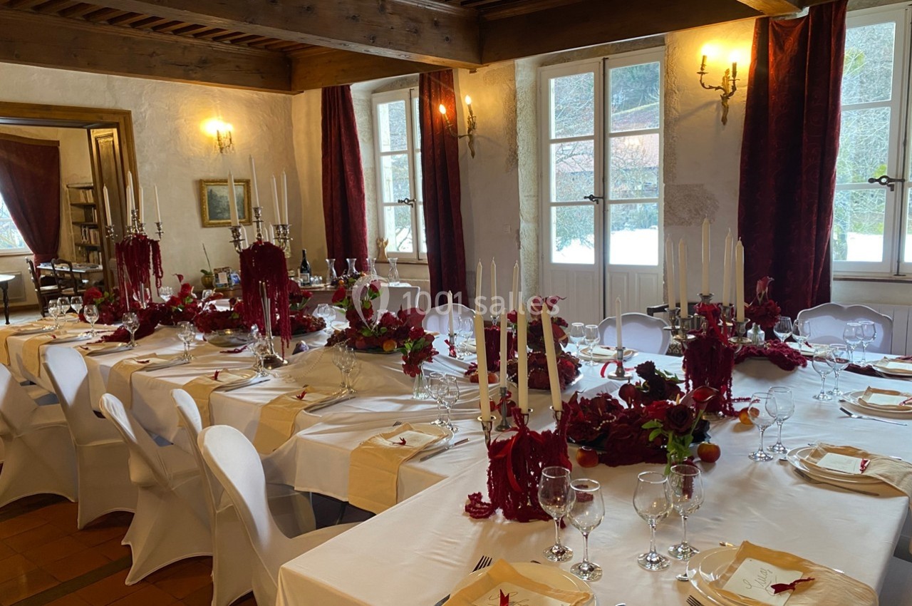 Salle de réception décorée avec des tables élégantes, nappes blanches, bougies et ornements rouges.