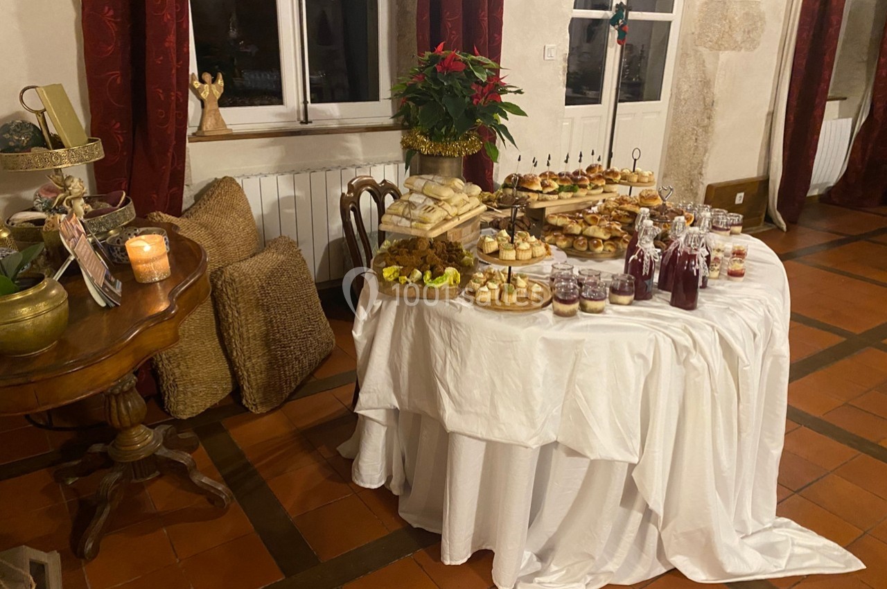 Table ronde décorée avec nappes blanches, garnie de plats variés, boissons et desserts dans une pièce chaleureuse.