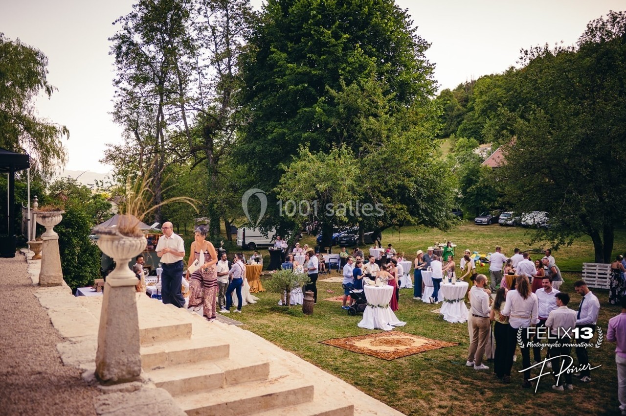 Groupe de personnes réunies dans un jardin pour un événement en plein air, avec tables hautes et décorations.
