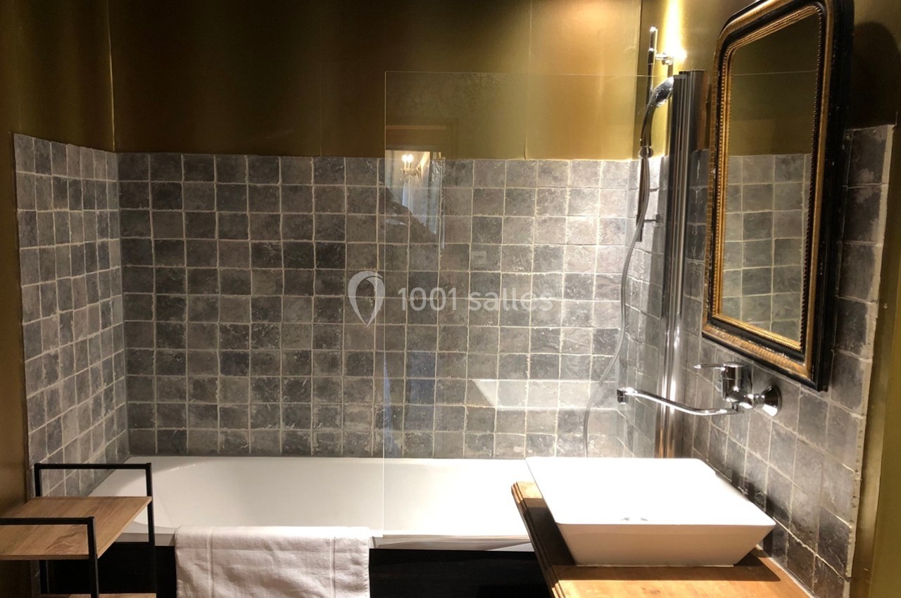 Salle de bain avec baignoire, paroi vitrée, lavabo sur meuble en bois et miroir encadré doré.