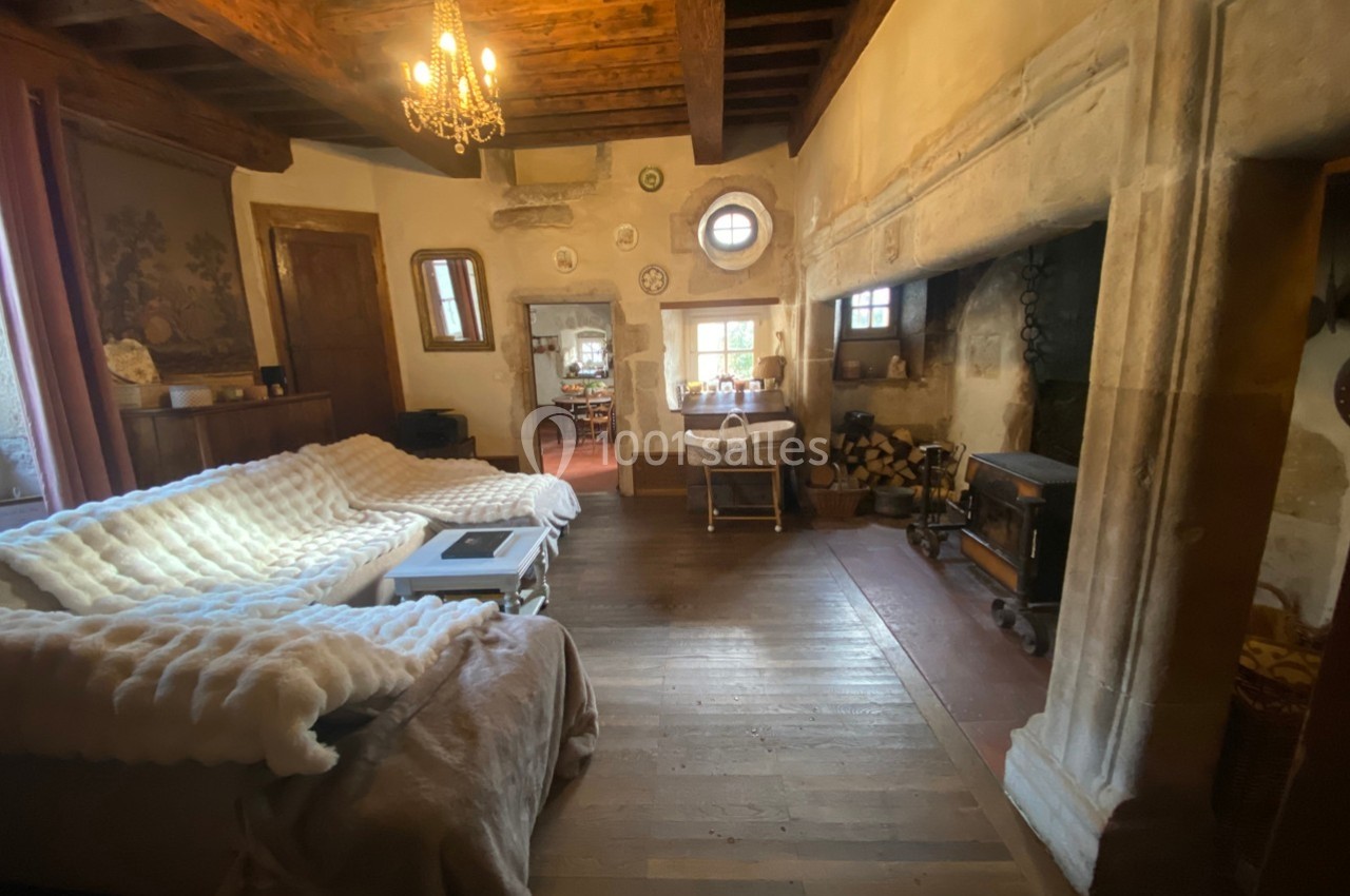 Salon rustique avec poutres apparentes, cheminée en pierre, canapé couvert d’un plaid et lumière naturelle.
