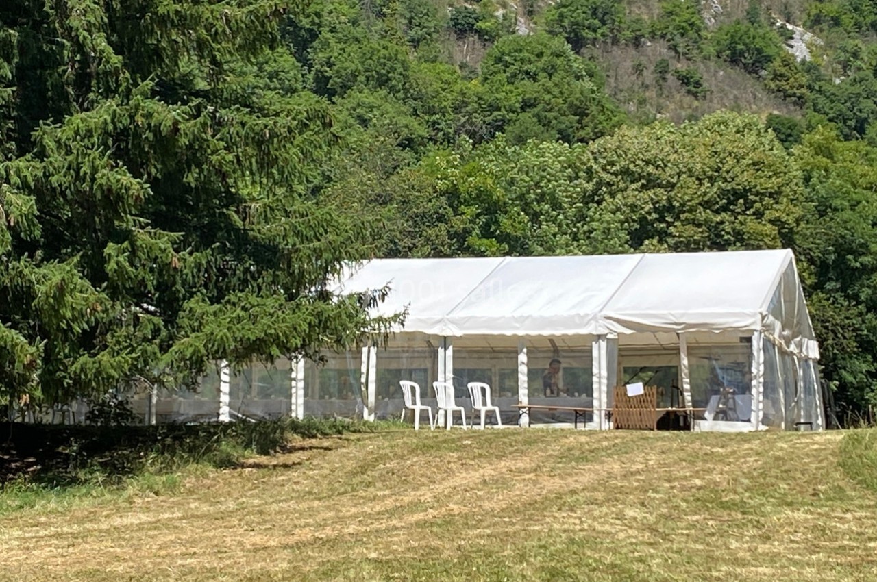 Tente blanche installée sur une pelouse, entourée d'arbres et de collines verdoyantes en arrière-plan.